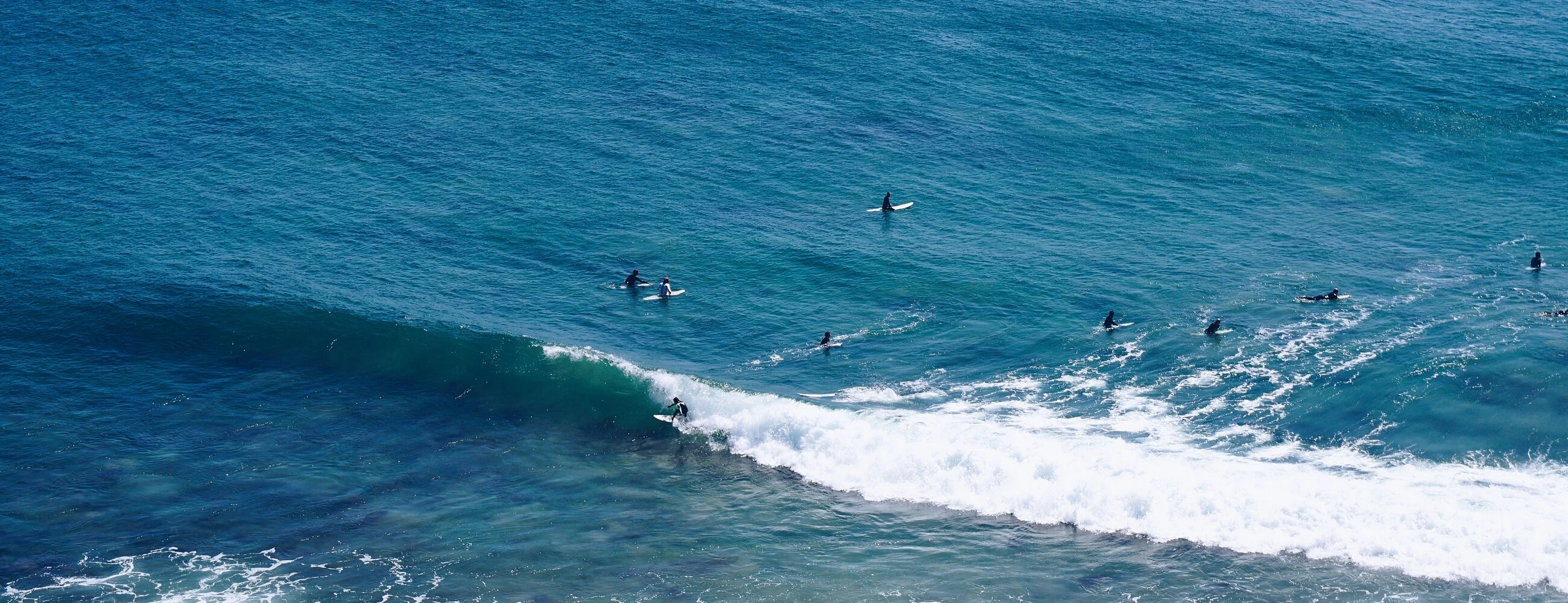 Surfers in the lineup at Zuma Beach, Malibu — one up and riding a peeling left